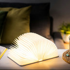 Gingko Design – Lámpara Smart Book LED - Lino Gris Urbano - 2 Tamaños, lámpara libro abierta y encendida en una mesita de noche, ambiente acogedor