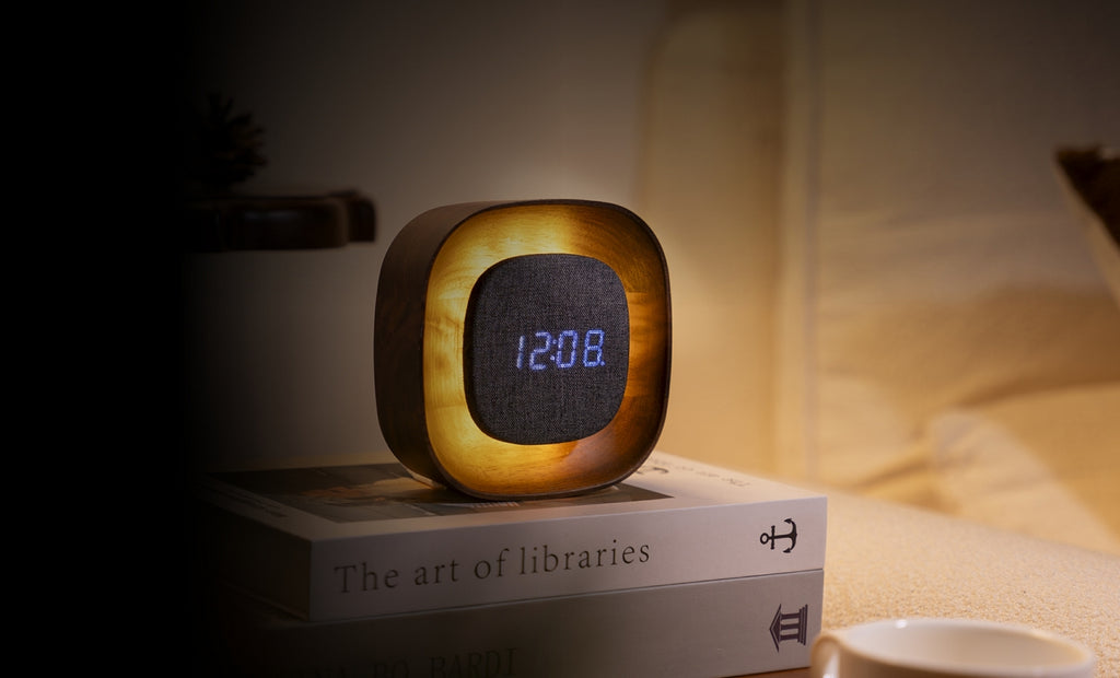 Gingko Design – Orologio Lumos - Quadrata Noce, sveglia luminosa posata su dei libri, che indica l'ora in una camera da letto