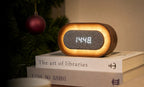 Gingko Design – Lumos Uhr - Oval Walnuss, Wecker aus Holz und grauem Stoff auf Büchern mit einem Weihnachtsbaum