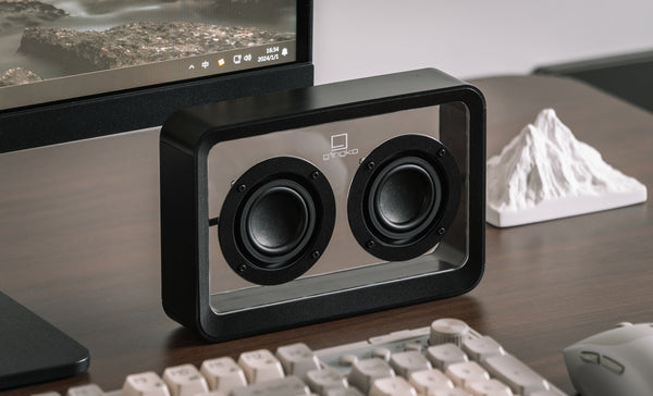 Gingko Design – Altavoz Mage Bluetooth Transparente - Madera Negra, altavoz bluetooth transparente colocado sobre un escritorio de madera