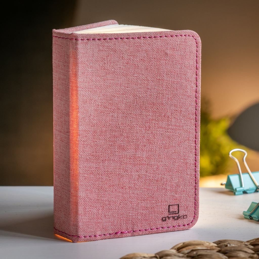 Gingko Design – Lampe Smart Book LED - Lin Rose Poudré - 2 Tailles, livre lumineux rose posé sur une table, ambiance chaleureuse