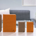 Gingko Design – Lampada Smart Book LED - Lino Marrone Caffè - Mini, quattro taccuini di dimensioni e colori diversi posati su un tavolo