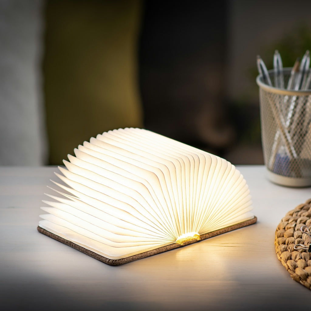 Gingko Design – Lampada Smart Book LED - Lino Marrone Caffè - Mini, lampada a forma di libro aperto, posata su un tavolo in legno chiaro