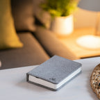 Gingko Design – Lámpara Smart Book LED - Lino Gris Urbano - 2 Tamaños, libro gris colocado sobre una mesa de centro en un salón