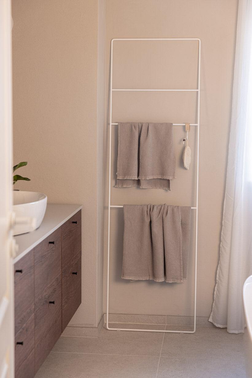 Helles Badezimmer mit Handtuchleiter Estina, auf der zwei graue Handtücher hängen.