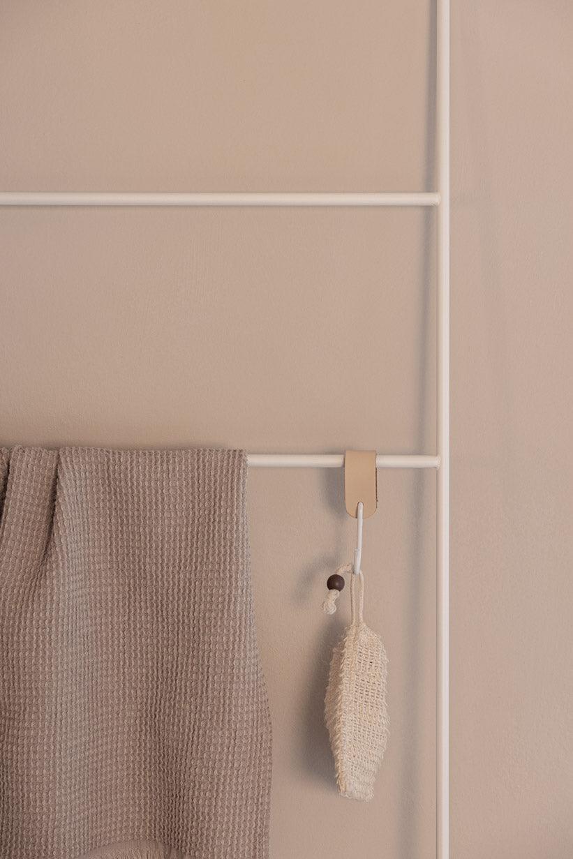 Handtuchleiter ESTINA mit einem beige Handtuch und einem natural Reinigungsschwamm an einer white Wand.
