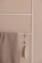 Handtuchleiter ESTINA mit einem beige Handtuch und einem natural Reinigungsschwamm an einer white Wand.