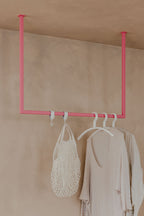 Kleiderstange RUBI en diseño minimalista con un gesto rosa, ideal para Ankleidebereiche, mit Kleidern y Tasche.