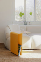Beistelltisch COSMO in modernem Design mit gelber Oberfläche neben einem Sofa platziert, ideal für Getränke und Bücher.