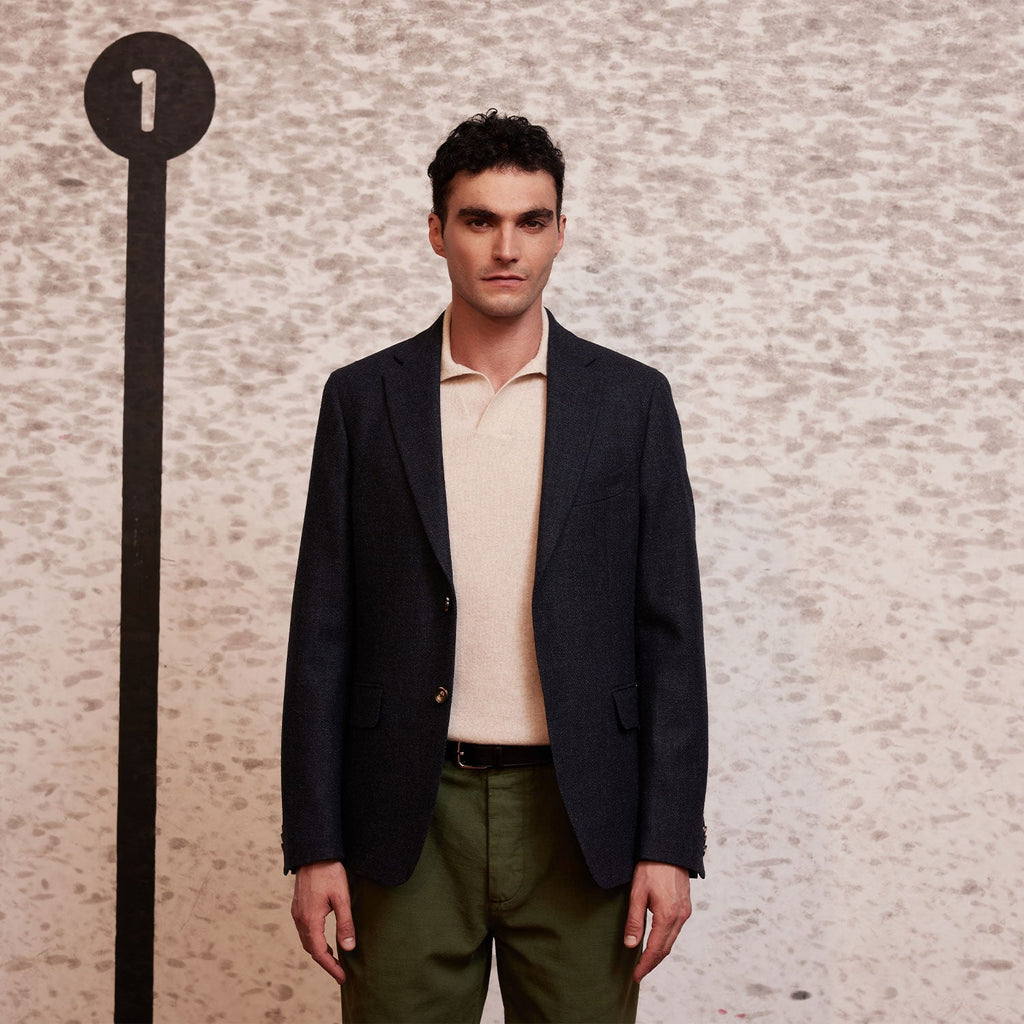 Hast – Melerad Blå Kavaj I Ren Ny Ull, manlig modell bärande en marinblå blazer och en beige pikétröja