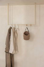 Kleiderstange RUBI mit Kleidungsstücken und einer Tasche an der Wand, diseño minimalista para Ankleidebereiche.