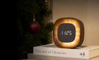 Gingko Design – Orologio Lumos - Quadrata Noce, sveglia luminosa posata su dei libri, con un albero di Natale sullo sfondo
