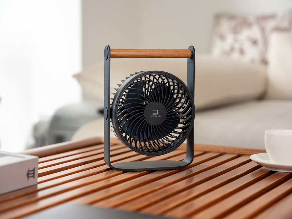 Gingko Design – Ventilatore Portatile Lyra - Grigio Siderale, piccolo ventilatore nero e legno appoggiato su un tavolo in legno