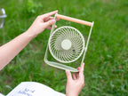 Gingko Design – Ventilatore Portatile Lyra - Grigio Siderale, una persona tiene un piccolo ventilatore verde chiaro in un giardino