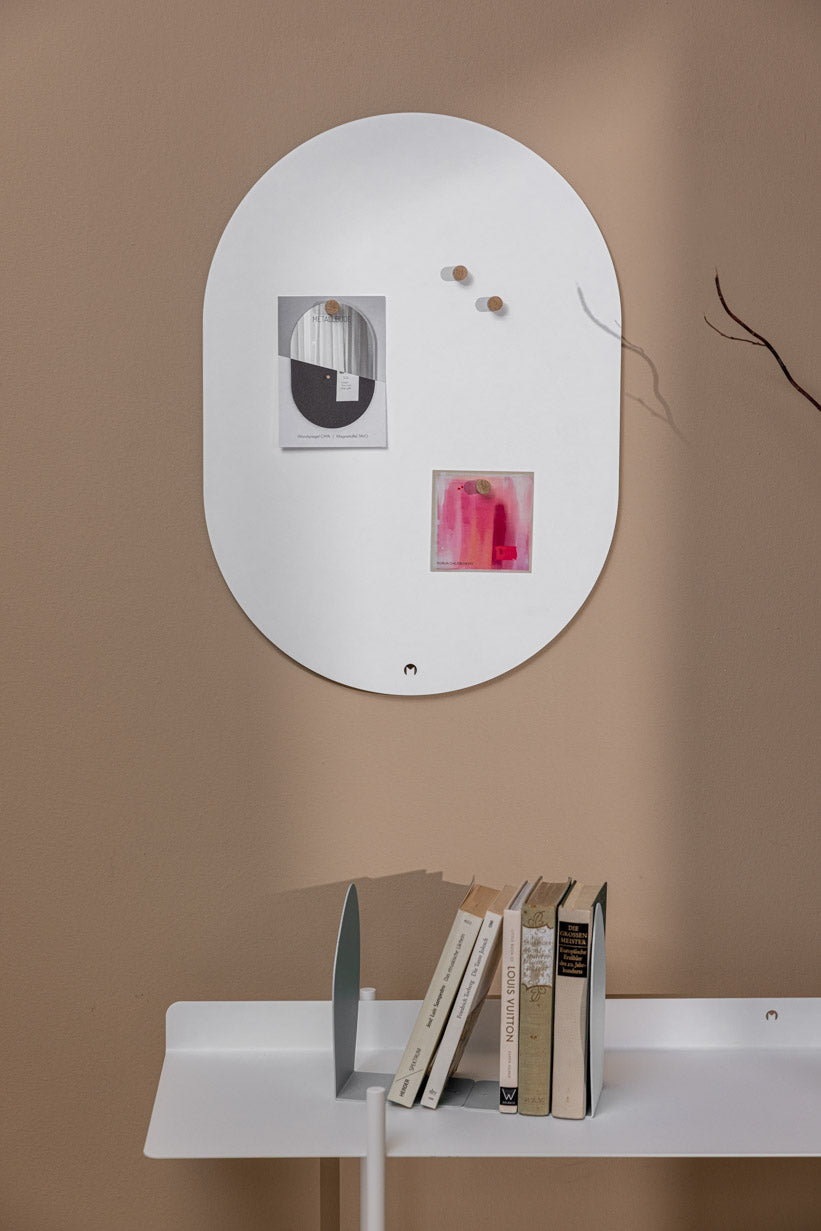 Elegante Magnettafel TAVO an der Wand mit Notizen und Büchern auf dem Tisch darunter.