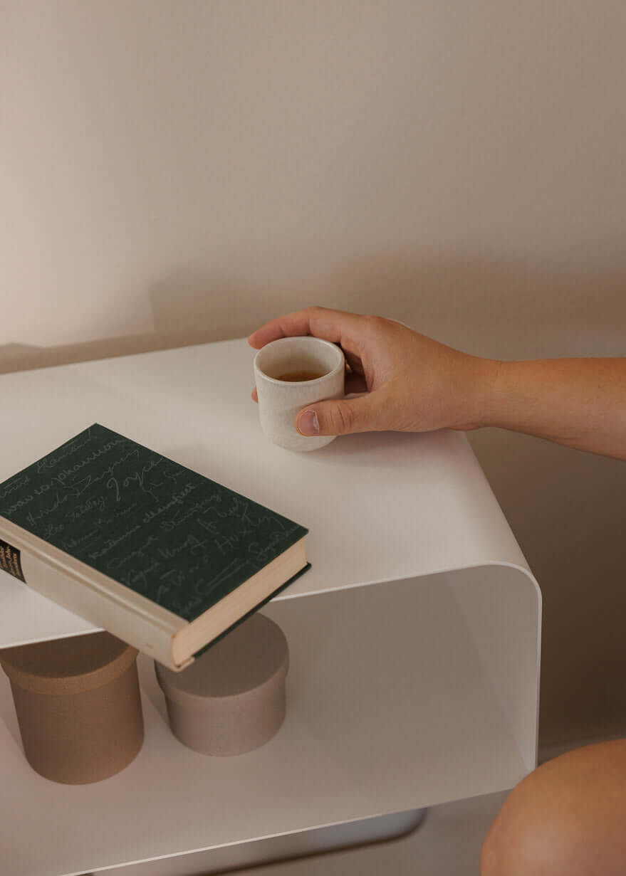 Stehender Nachttisch mit einem Buch und einer Tasse auf der fläche, elegancia minimalista en estilo moderno.