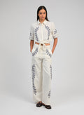 An'ge – Rossalie Trousers Ecru, model wearing a white co-ord set embroidered with blue botanical motifs, front view