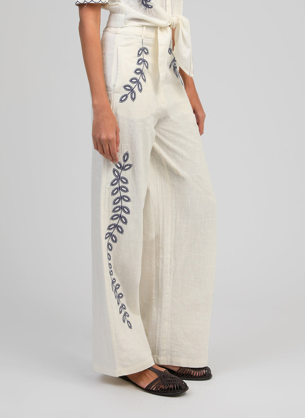 An'ge – Rossalie Trousers Ecru, off-white wide-leg trousers embroidered with blue botanical motifs, worn from the side