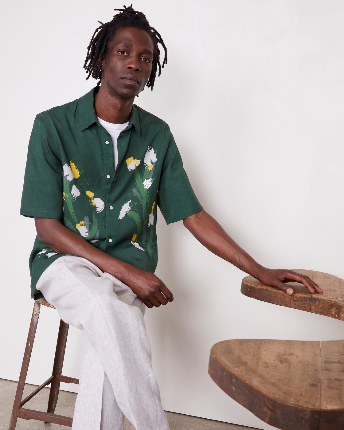 Officine Générale – Chemise Eloi Manches Courtes - Vert Pin/Vert Laitue/Gris - Homme, mannequin homme assis, chemise verte à fleurs, pantalon clair