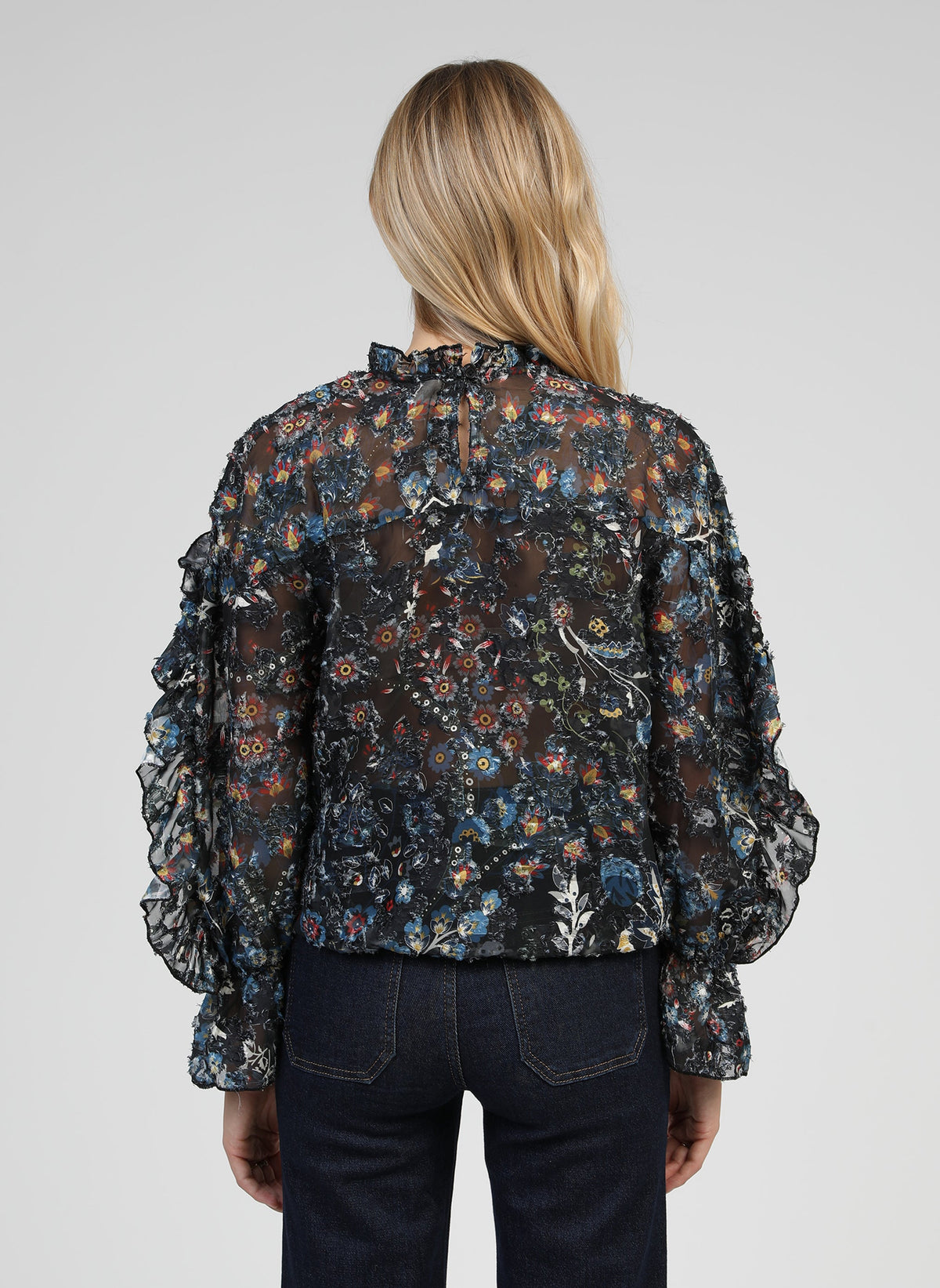 An'ge – Blouse Soelina Folina Noir, model op de rug gezien in een zwarte blouse met bloemenprint en ruches