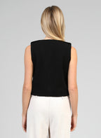 An'ge – Chaqueta Soleda Negro, modelo de espaldas con top negro sin mangas y pantalón claro