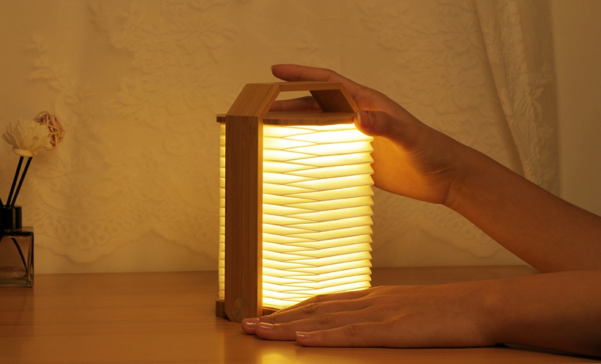 Gingko Design – Lámpara Smart Origami - Bambú Natural, lámpara plegable de madera clara y papel, colocada sobre una mesa de madera