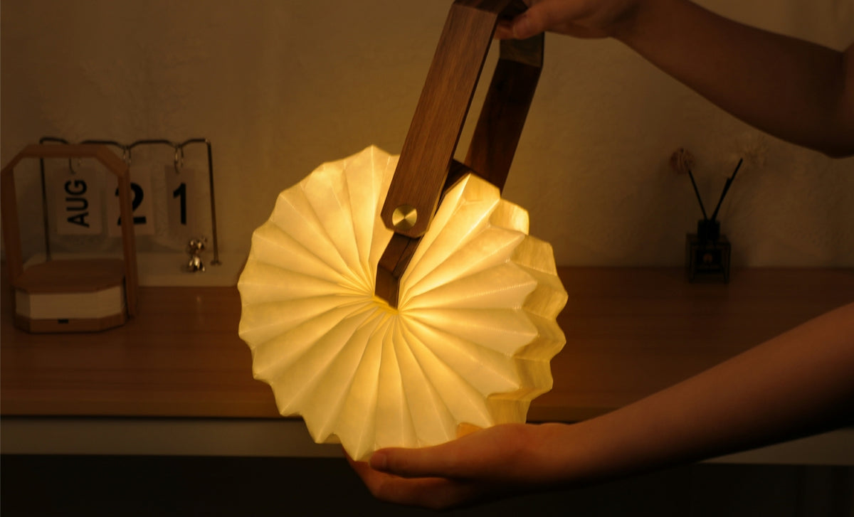 Gingko Design – Lámpara Smart Origami - Bambú Natural, lámpara plegable de madera y papel plisado, sostenida por dos manos