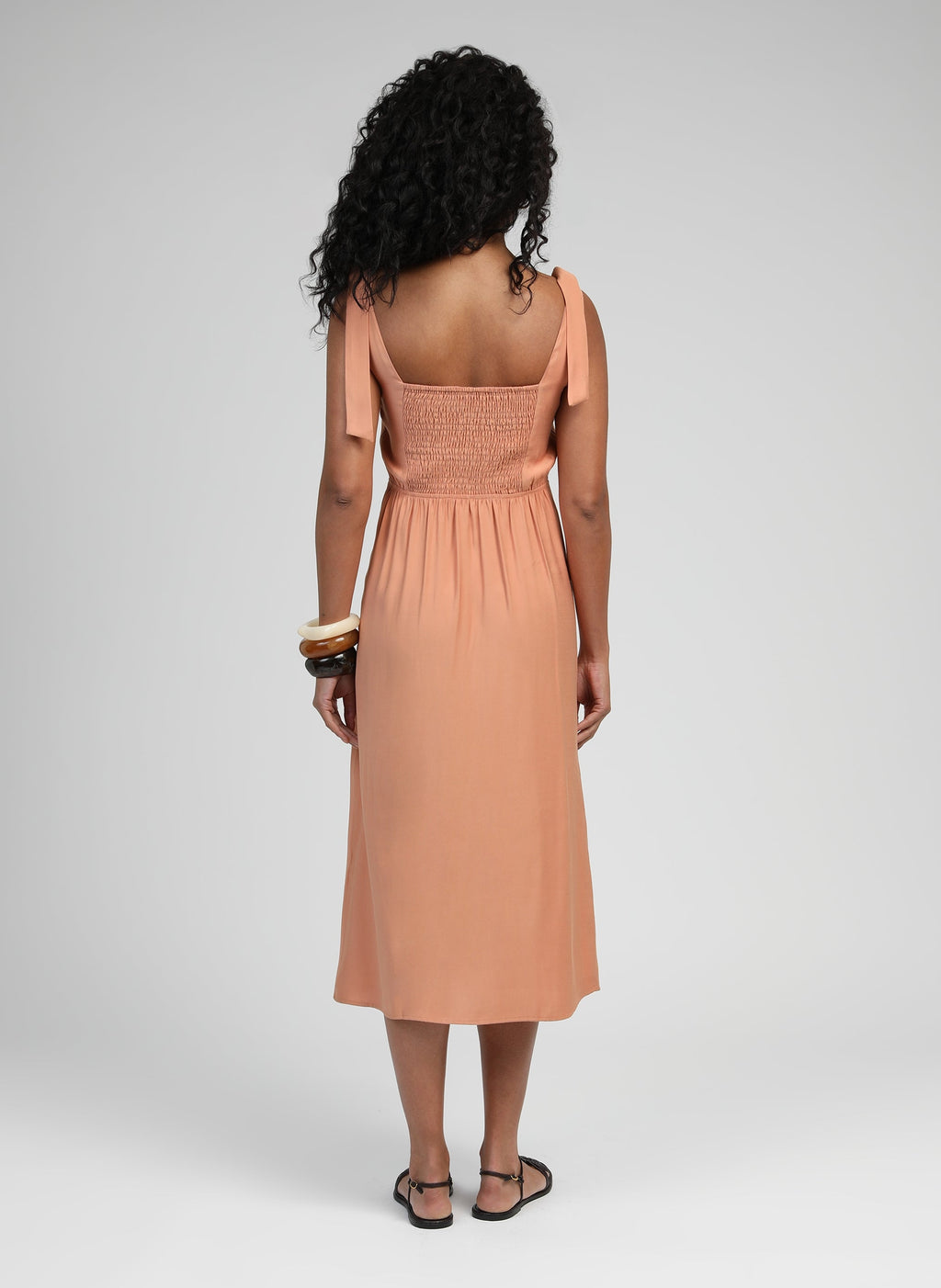 An'ge – Robe Midi Manta Terracotta, model set bagfra iført en ferskenfarvet maxikjole med sandaler