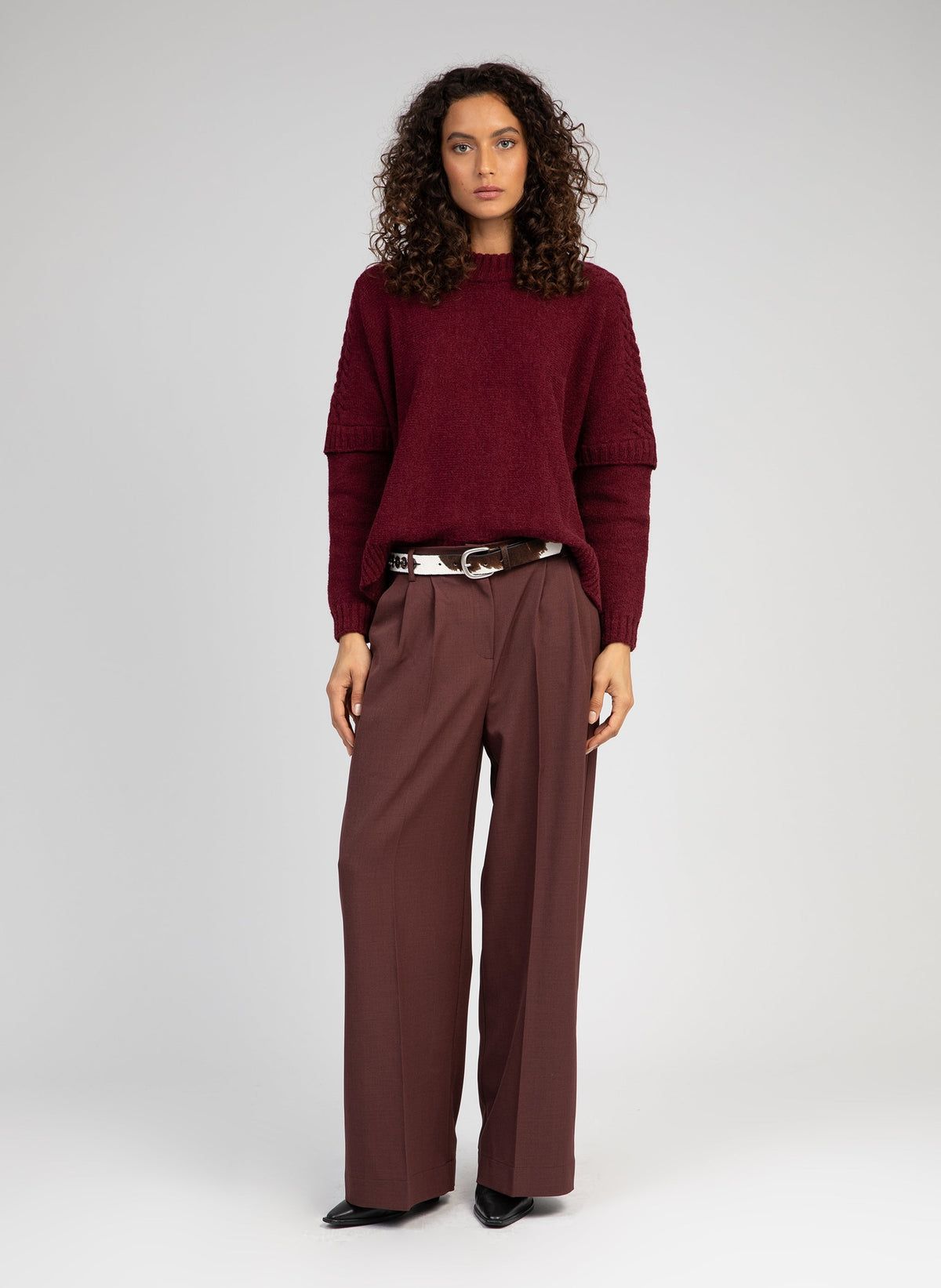 An'ge – Pantaloni Pepina Chocolat, modella che indossa un maglione bordeaux e pantaloni marroni con cintura