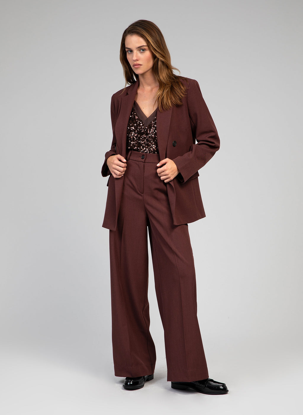 An'ge – Hose Perlina Schokolade, Model im braunen Anzug aus Blazer und Hose mit einem Pailletten-Top