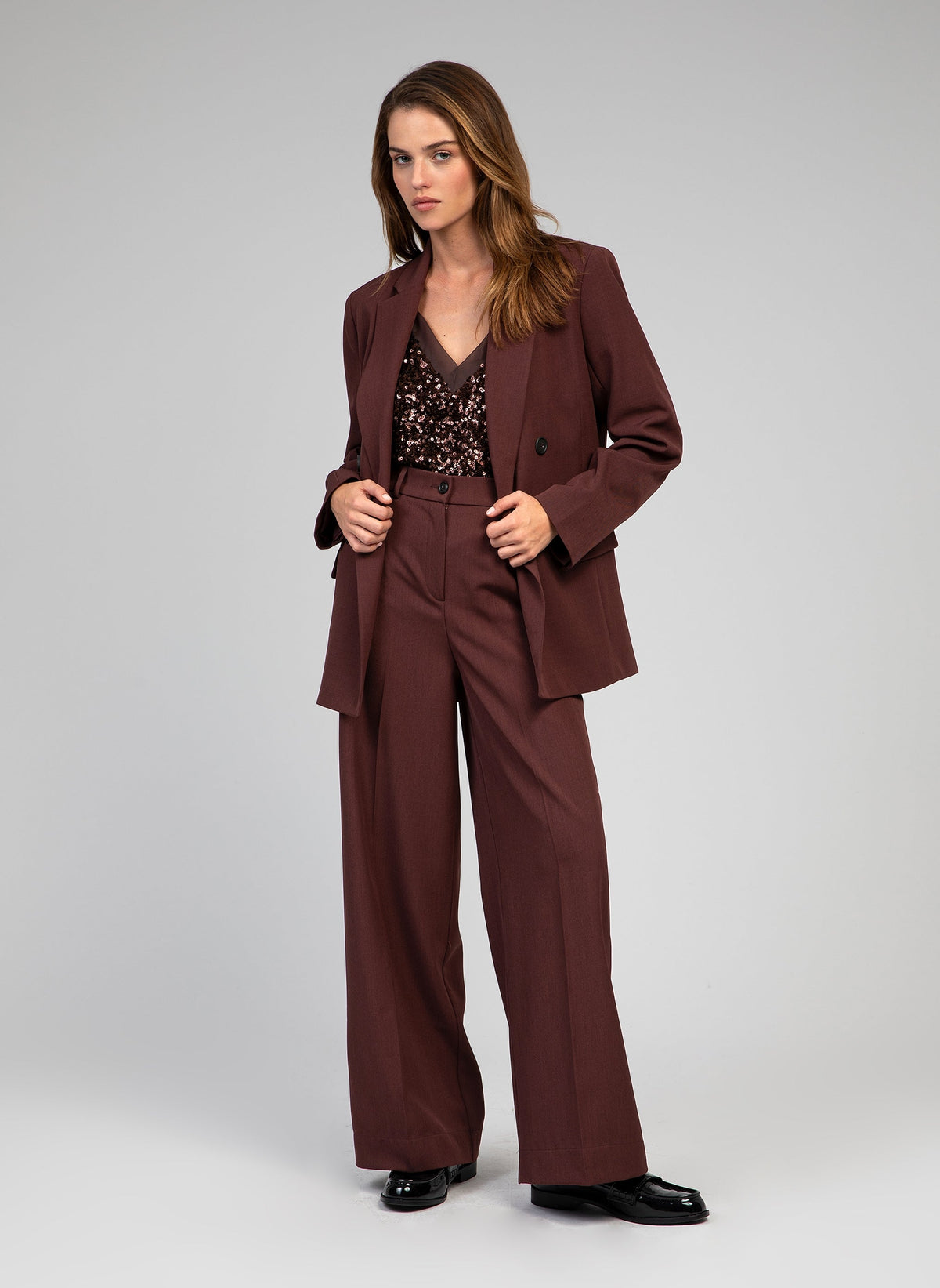 An'ge – Hose Perlina Schokolade, Model im braunen Anzug aus Blazer und Hose mit einem Pailletten-Top